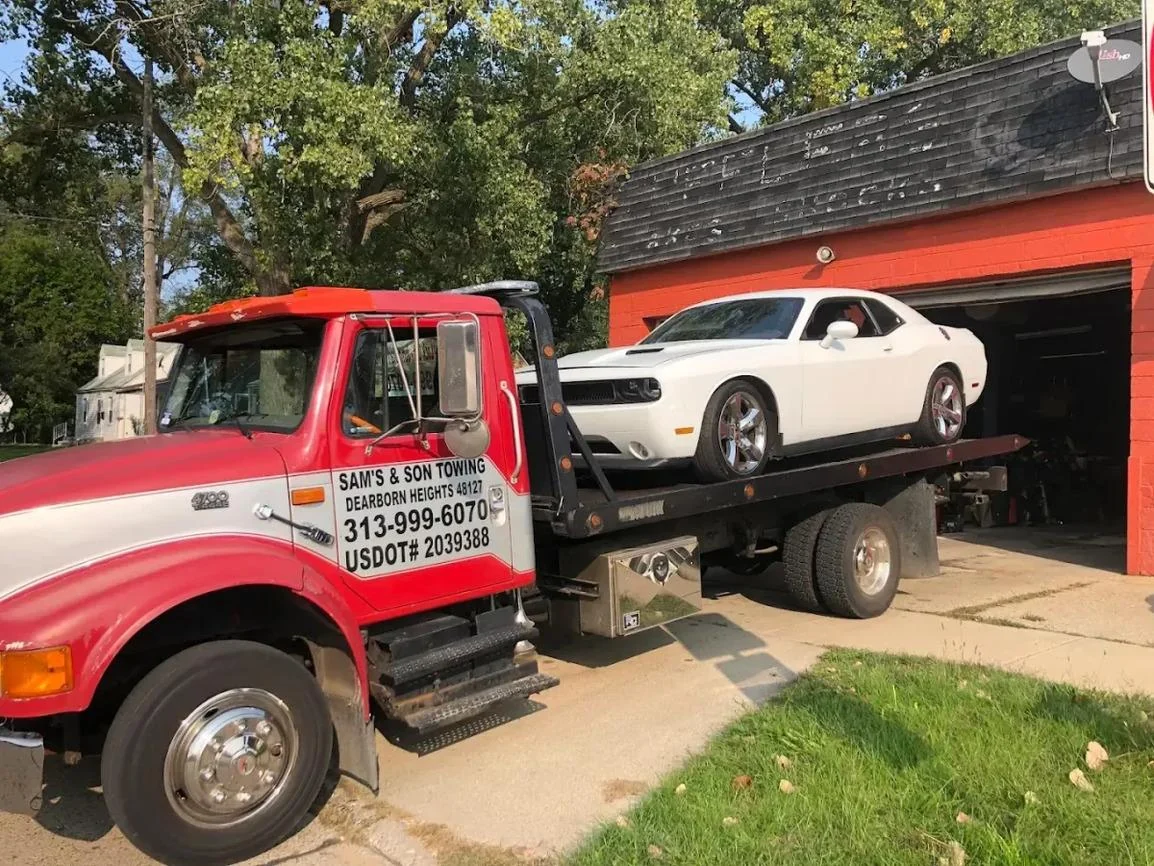 White coupe on the red flatbed outside a repair garage