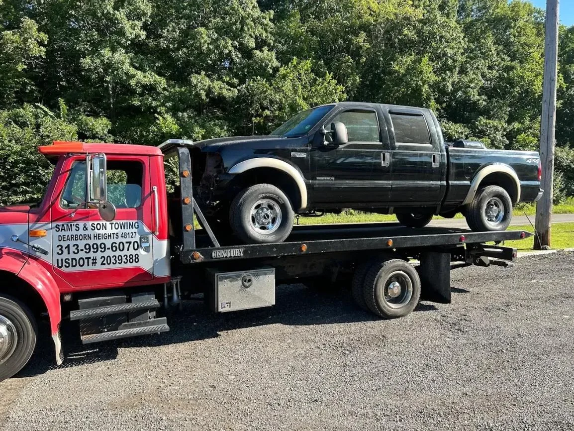 Sam's & Son's red flatbed tow truck carrying a black pickup