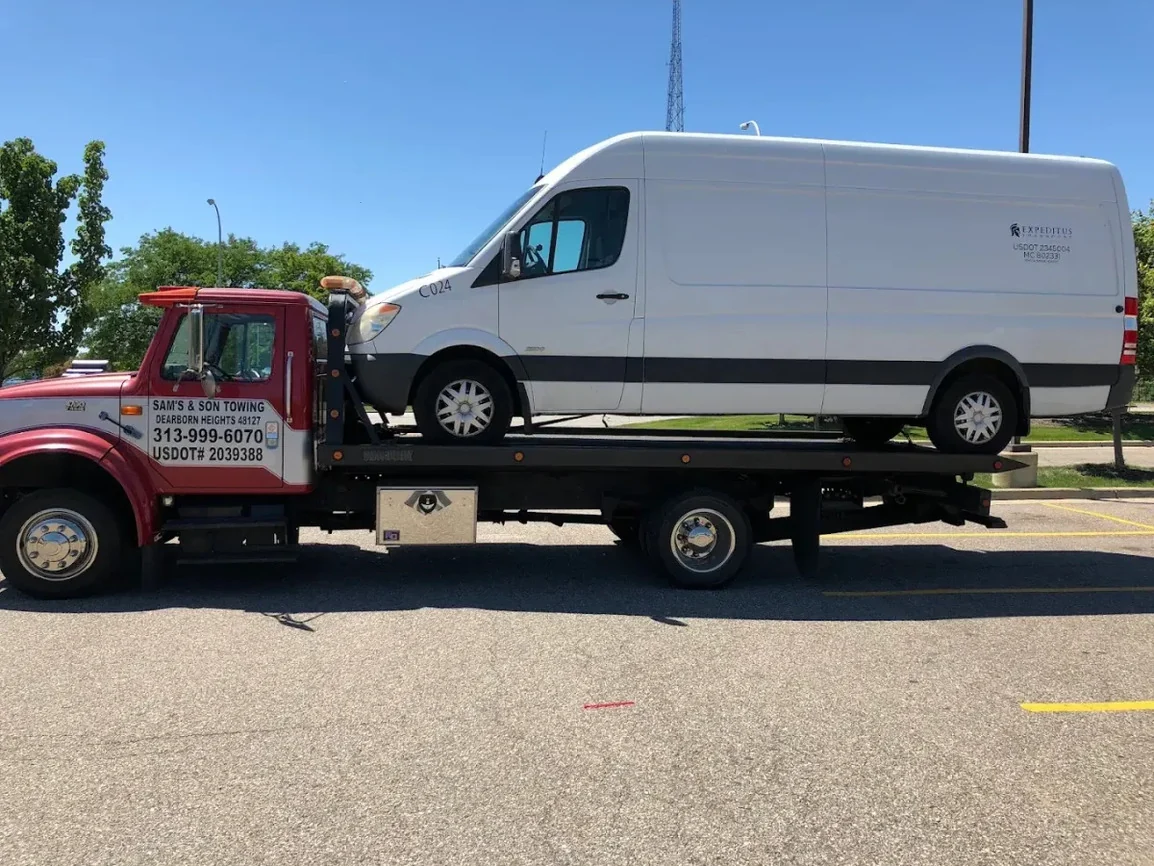 A white cargo van secured on Sam's & Son's red flatbed